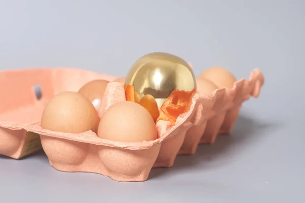 Картонна яєчна коробка з золотими та курячими яйцями на сірому фоні — стокове фото