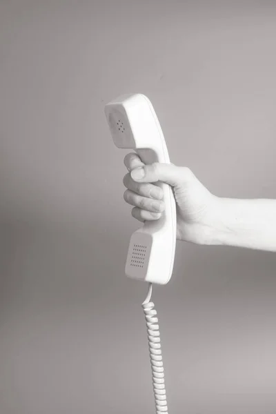 Mão segurando tubo de telefone branco no fundo cinza . — Fotografia de Stock