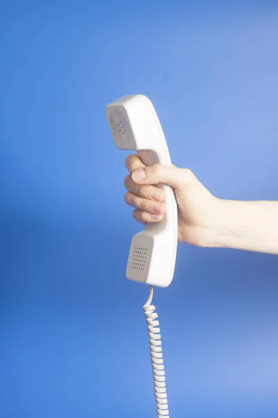 Рука держит белый телефон трубки на синем фоне — стоковое фото