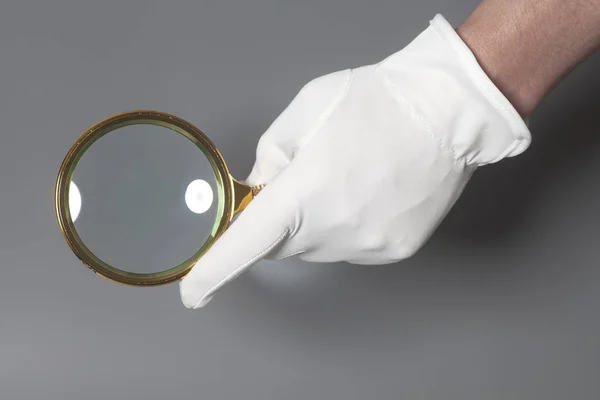 Mano de hombre en guante blanco con lupa dorada — Foto de Stock