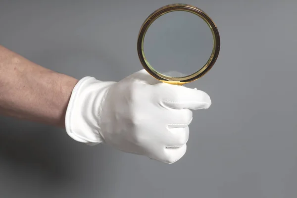 Mano de hombre en guante blanco con lupa dorada — Foto de Stock