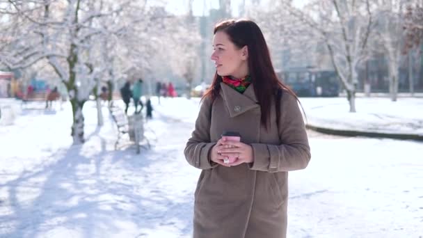 Bir ceket, bir genç kız kış parktan elini kolunu sallaya dönüyor ve kameraya bakarken kahve içer — Stok video