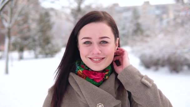 Egy fiatal lány, egy kabátot, séták a téli parkon keresztül, és iszik kávét, miközben nézi a kamerát — Stock videók