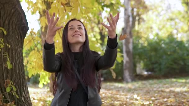 Retrato de una linda chica que vomita hojas amarillas en el parque de otoño y sonríe maravillosamente . — Vídeos de Stock