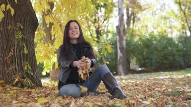 Portret van een schattig meisje dat in het najaarspark gele bladeren opgeeft en prachtig glimlacht. — Stockvideo