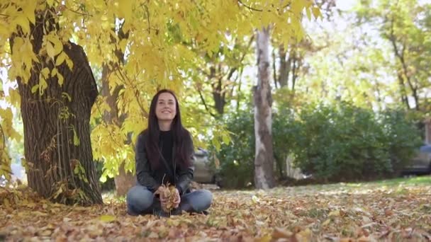 Porträtt av en söt flicka som kräks upp gula löv i höstparken och ler vackert. — Stockvideo