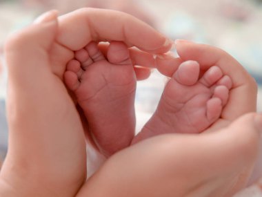 Bebek ayakları annenin ellerinde. Minik Yeni Doğmuş Bebek 'in ayakları, Kadın Kalp Şeklinde Eller, yakın plan. Annesi ve çocuğu. Mutlu Aile kavramı. Anneliğin güzel kavramsal fotoğrafı.