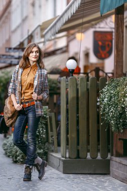 Moda kız mavi jeans, kahverengi kareli ceket giymiş ve elinde bir kahverengi çanta, Kentsel şehir kaldırımda yürüyor