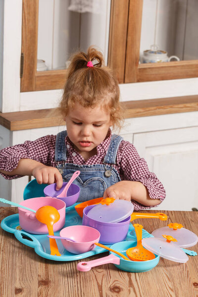 маленькая девочка играет игрушечные детские блюда дома
