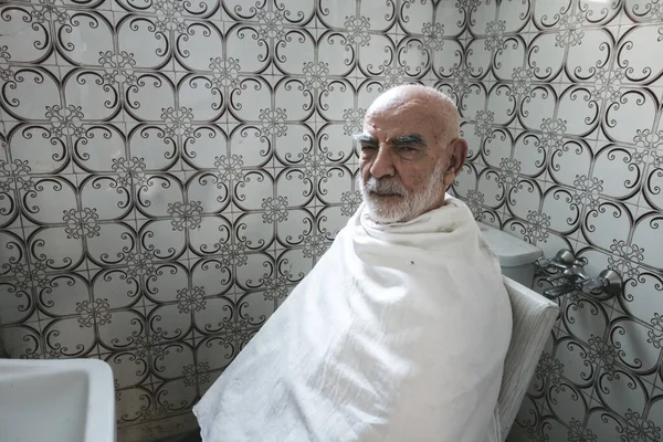 Yaşlı adam banyoda saç kesimini bekliyor.