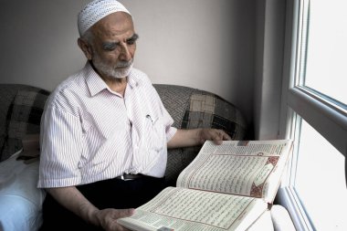 Takiyeli bilge yaşlı adam penceresinin önünde Kuran 'ı Türkçe çevirisini, İslam' ın kutsal kitabını okuyor.