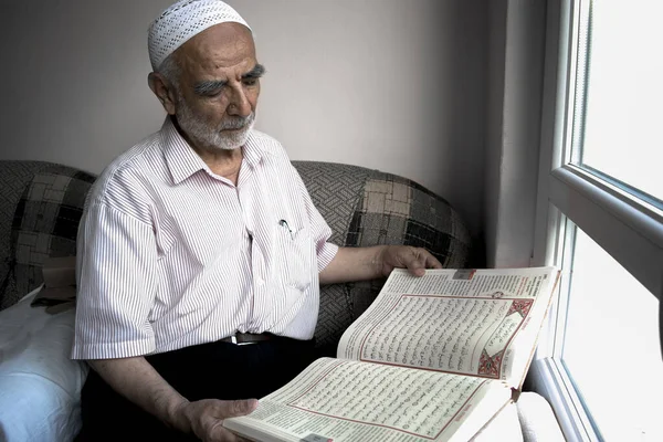 Takiyeli bilge yaşlı adam penceresinin önünde Kuran 'ı Türkçe çevirisini, İslam' ın kutsal kitabını okuyor.