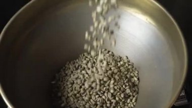 Taze çiğ kahve çekirdekleri kızartma makinesine dökülüyor.