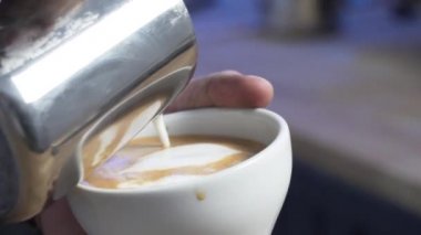 Barista bir fincan kahveye süt dökerek Latte sanatı yaratıyor.