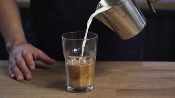 Pouring milk over a glass cup of coffee and ice — Stock Video
