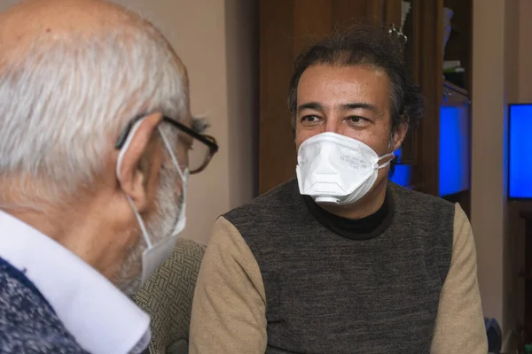 Maske takan kıdemli bir adam yaşlılarla konuşuyor.
