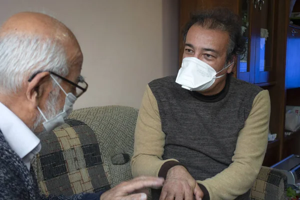 Maskeli kıdemli bir adam yaşlı bir adama evinde ellerini nasıl doğru dürüst yıkayacağını gösteriyor.