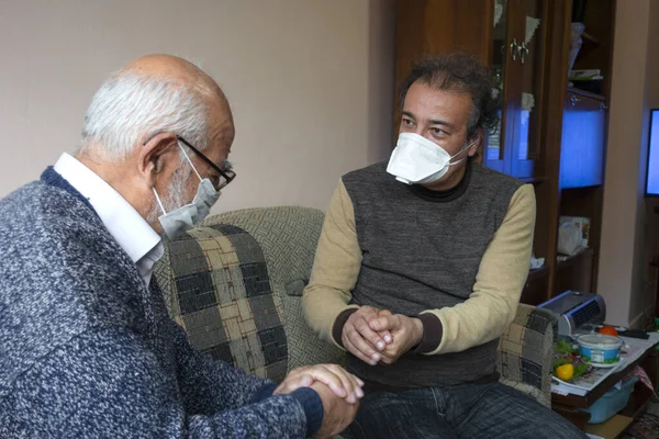 Maskeli kıdemli bir adam yaşlı bir adama evinde ellerini nasıl doğru dürüst yıkayacağını gösteriyor.