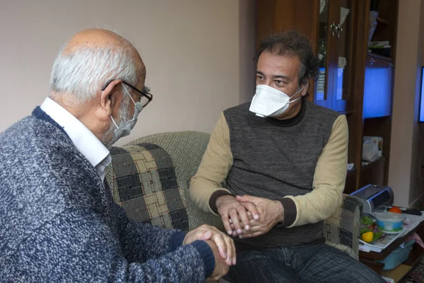 Maskeli kıdemli bir adam yaşlı bir adama evinde ellerini nasıl düzgün yıkayacağını söyler.