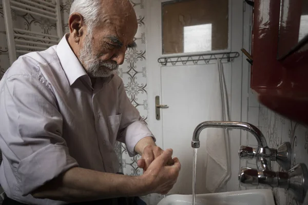 Çok yaşlı bir Türk adam, Coronavirus 'a karşı korunmak için ellerini banyoda yıkıyor.