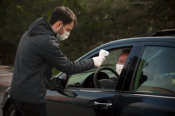 A Turkish security guy measuring a driver\'s body temperature with infrared thermometer both wearing surgical masks and gloves