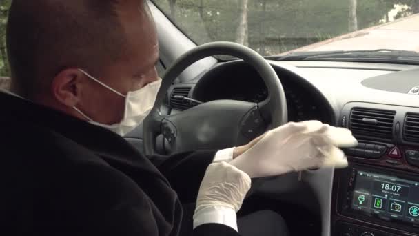 シニア男はCoid19に関する保護のために彼の車の中で彼の外科手袋を身に着けている — ストック動画