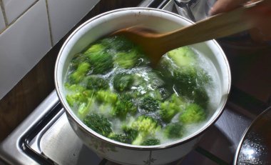 Kadın mutfak sobasında brokoli çorbası karıştırıyor. Tahta kaşık, sağlıklı yaşam, taze yeşil sebzeler.