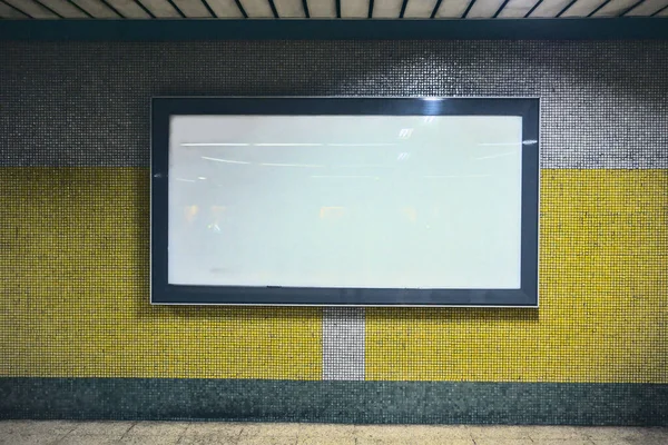 Metro koridorlarında sarı ve gri renkli bir duvara boş beyaz ilan panosu.