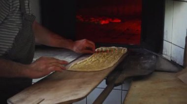 Fırıncı adam geleneksel Türk ramazan ekmeğine susam döker ve onu fırına koyar ve fırın küreğini kullanarak bir tane daha alır.