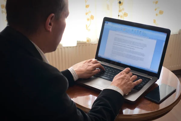 Zeki giyimli kıdemli akademisyen güneşli bir günde laptopundan bir makale yazarak evde çalışıyor.