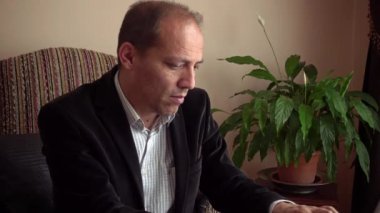 Ciddi zeki, son sınıf öğrencisi, şık kıyafetler giyen, arka planda bir bitki olan dizüstü bilgisayarla çalışan bir adam.