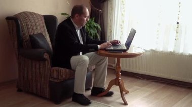Ciddi zeki, son sınıf öğrencisi, şık kıyafetler giyen, arka planda bir bitki olan dizüstü bilgisayarla çalışan bir adam.