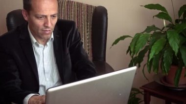Zeki kıdemli ciddi görünüyor. Bilgisayarını arka planda bir bitkiyle evde çalışıyor.