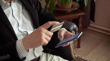 Zeki, yakışıklı, orta yaşlı bir adam kredi kartına bakıyor ve evden online alışveriş için telefonunun şifresini giriyor.
