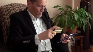 Zeki, yakışıklı, orta yaşlı bir adam kredi kartına bakıyor ve evden online alışveriş için telefonunun şifresini giriyor.