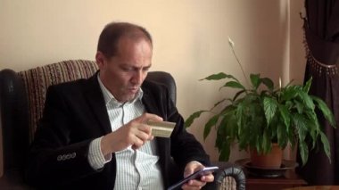 Akıllı yetişkin adam, şık kıyafetler giyiyor. Kredi kartı alışverişi yapıyor. Evde akıllı telefon kullanıyor.
