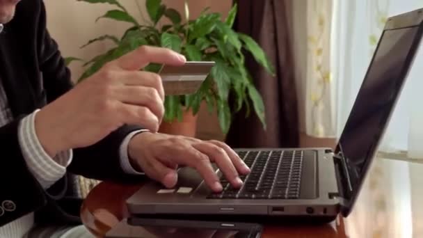 中年男人穿着漂亮的衣服 拿着信用卡上网购物 他在家里带着一台带背景音乐的笔记本电脑 — 图库视频影像