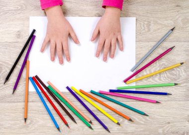 Çocuğun elleri ahşap zemin ile çevrili bir kağıt parçasına uzanır.