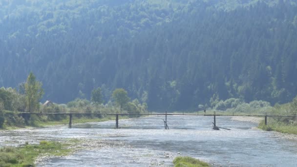 En man går över floden berg på en bro — Stockvideo