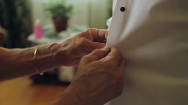 Las manos viejas de la madre sujetan la camisa al hijo joven — Vídeos de Stock