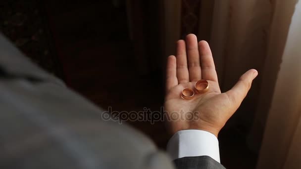 Man toont twee gouden ringen op zijn handpalm, dan is de samendrukking van de hand in een vuist — Stockvideo