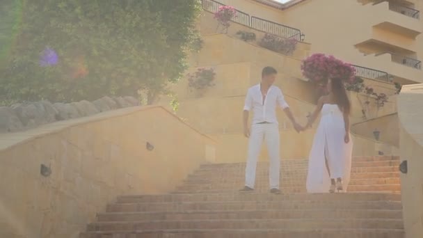 Молода пара йде вниз по сходах у білій сукні, сонце світить — стокове відео