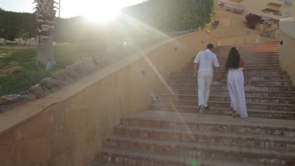 这对年轻夫妇走在楼梯上穿白色连衣裙，在太阳的照耀 — 图库视频影像