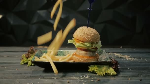 Hamburguesa fresca y apetitosa y papas fritas cayendo, fondo negro, dolly shot — Vídeos de Stock