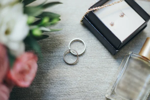 Hermosos anillos de boda se encuentran en una mesa el fondo de un ramo de flores — Foto de Stock