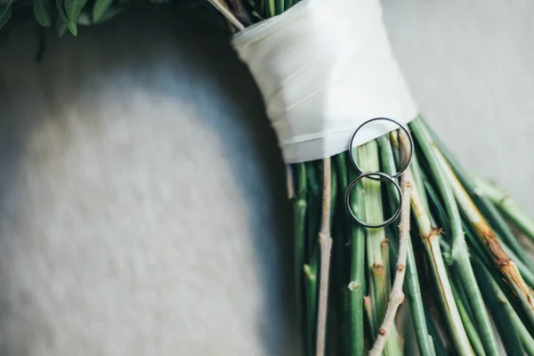 Los anillos de boda sobre la mesa el fondo del ramo de flores — Foto de Stock