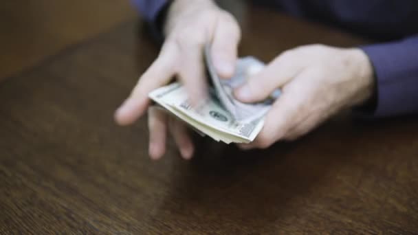 Un homme d'affaires compte des billets de cent dollars sur une table en bois — Video