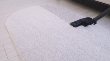 Ev içinde bir kaplamanın üzerindeki halıyı temizlemek için elektrikli süpürge kullanan bir kadın.