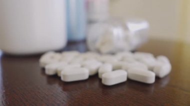 White pills on the table, slowly approaching the bottle, focus on macro close up