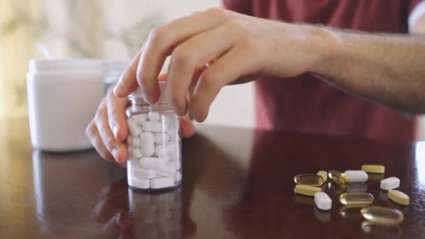 Primeros planos toma comprimidos blancos de vitaminas y medicamentos sentados a la mesa — Vídeo de stock